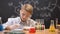 Schoolboy looking at sediment in flask and writing results, chemistry lesson