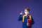 Schoolboy in mask, in uniform with book and backpack on purple background