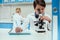 Schoolboy with microscope and copybook in science laboratory