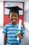 Schoolboy in mortar board holding certificate in classroom