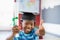 Schoolboy in mortar board holding certificate and showing thumbs up in classroom