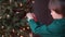 A schoolboy puts a New Year toy, a ball, on a Christmas tree.