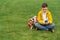 Schoolboy sits on the lawn with  smart phone in his hands. Modern teenager in yellow jacket.