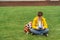 Schoolboy sits on the lawn with  smart phone in his hands. Modern teenager in yellow jacket.