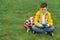 Schoolboy sits on the lawn with  smart phone in his hands. Modern teenager in yellow jacket.