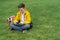 Schoolboy sits on the lawn with  smart phone in his hands. Modern teenager in yellow jacket.