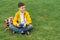 Schoolboy sits on the lawn with  smart phone in his hands. Modern teenager in yellow jacket.