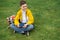 Schoolboy sits on the lawn with  smart phone in his hands. Modern teenager in yellow jacket.