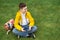 Schoolboy sits on the lawn with  smart phone in his hands. Modern teenager in yellow jacket.