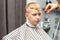 A schoolboy is sitting in a barbershop, doing his hair with scissors for haircuts