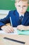 Schoolboy sitting at desk at school and writing to notebook