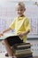 Schoolboy Sitting On Stack Of Books