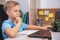 Schoolboy studies at home while sitting at table in front of laptop