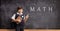 Schoolboy in a uniform with books pointing to a blackboard with math formulas