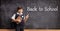 Schoolboy in a uniform holding books and pointing to a blackboard with text back to school