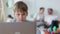 Schoolboy using laptop and sitting at table while learning online at home, parents are behind spbi.