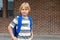 Schoolboy walking to school, carrying backpack. Student against brick wall of school building with copy space