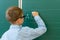 schoolboy writes the letters A,B,and C in chalk on a green blackboard.