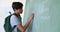 Schoolboy writing on green chalkboard in classroom