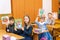 Schoolboys and schoolgirls sitting at their desks show textbooks to teacher holding them over their heads