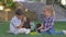 Schoolchildren chat during recess lunch with sandwiches in hands sitting on grass in schoolyard