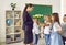 Schoolchildren congratulating their female teacher and giving her flowers in school classroom.