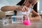 A schoolgirl conducts experiments in a chemistry lesson. Girl pouring colored liquids from a beaker.