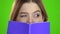 Schoolgirl covered her face with a violet notebook . Green screen. Close up