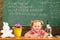 Schoolgirl do homework assignment on chalkboard background. Little child do homework at desk