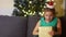 Schoolgirl in an elegant green dress and headband with a Santa hat opens a gift. The girl is very surprised and