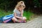 Schoolgirl of elementary school sits having crossed legs on a grass and something writes to notebook.