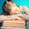 Schoolgirl fell sleep on a stack of books. ing a book on blue background
