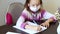 Schoolgirl girl in mask studying, writing homework at home, social distance during quarantine coronavirus,