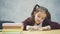 A schoolgirl girl sits on a gray background. During this time the schoolboy reads the book carefully. Diligent student