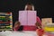 Schoolgirl hiding face behind book against black background