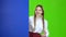 Schoolgirl looks out from behind a blue board and shows a thumbs up. Green Screen