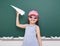 Schoolgirl with paper plane play near a blackboard, empty space, education concept