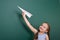 Schoolgirl with paper plane play near a blackboard, empty space, education concept