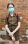 Schoolgirl poses against a brick wall in the backyard of the school, wearing a protective mask on her face from a coronavirus