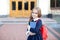 schoolgirl of primary school on way to study. Beginning of lessons. Little girl outdoors near school building. Schoolgirl with a b