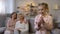 Schoolgirl putting coin in piggybank, proud mother and granny behind, savings