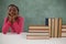 Schoolgirl sitting beside books stack against chalkboard