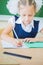 Schoolgirl sitting at desk at school and writing to notebook