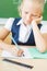 Schoolgirl sitting at desk at school and writing to notebook