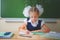 Schoolgirl sitting at desk at school and writing to notebook