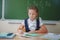 Schoolgirl sitting at desk at school and writing to notebook