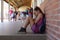 Schoolgirl sitting on the ground against a wall alone in the schoolyard at elementary school