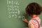 Schoolgirl solving maths formula on green board in classroom