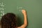 Schoolgirl solving maths formula on green board in classroom