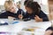 Schoolgirl using a tablet and stylus sitting with a boy at a desk in a primary school classroom, selective focus